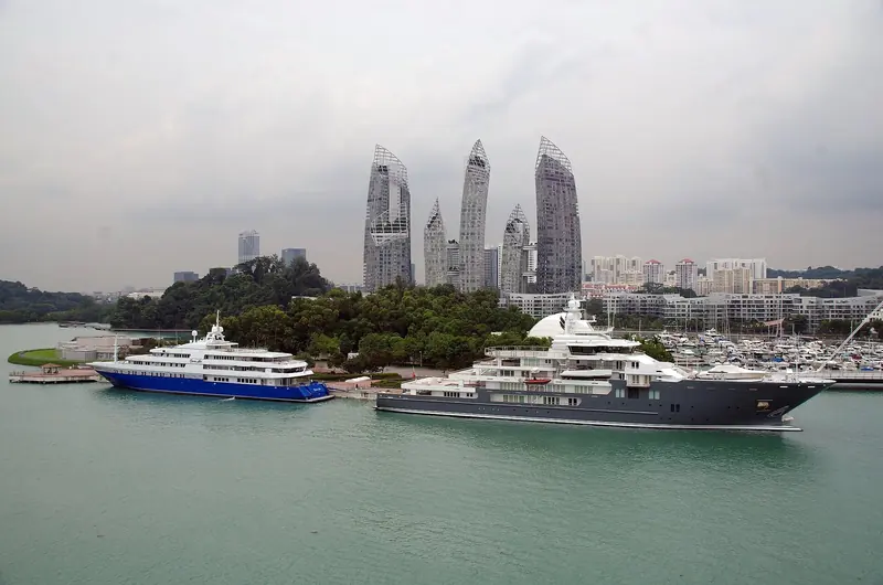 Two large motoryachts moored off the point, with the Reflections at Keppel Bay towers and the wider marina basin behind them.