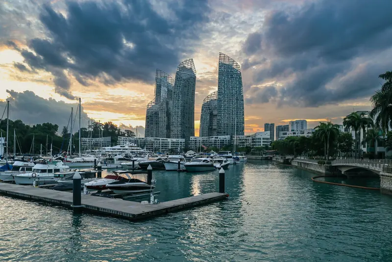 Berthed motorboats and sailboats at dusk, the part-clad Reflections at Keppel Bay towers still under construction rising behind the marina.