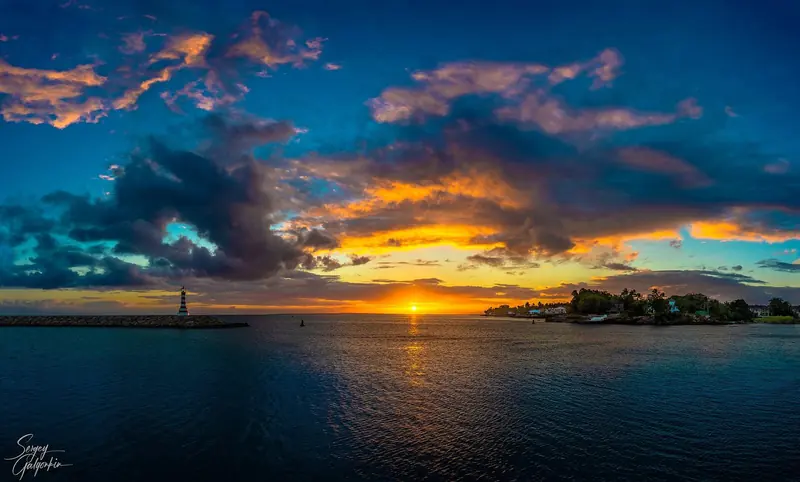 The striped lighthouse on the breakwater at the marina entrance, La Romana, at sunset.