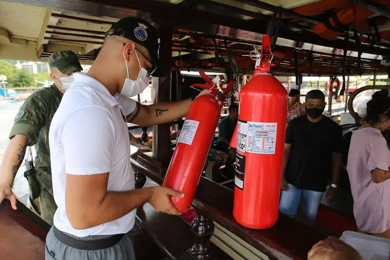 A Brazilian Navy maritime safety officer inspects a tour boat's fire extinguishers at Marina da Gloria, part of the routine vessel checks the port authority runs on the marina's excursion fleet.