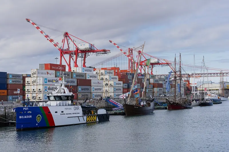 The GNR patrol vessel Bojador and the tall ships Vera Cruz and Atyla moored at the commercial quay beside Doca de Alcantara, container cranes and the 25 de Abril bridge behind.