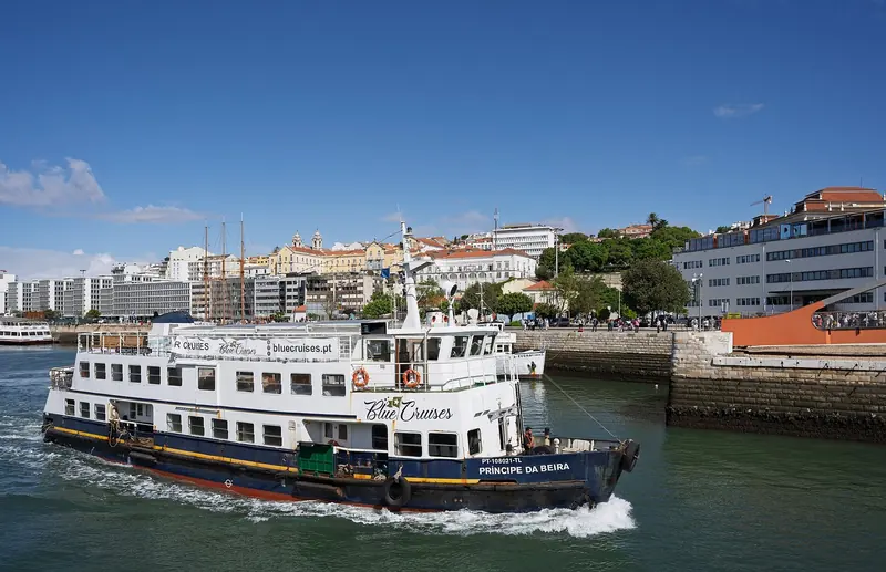 The tour boat Principe da Beira, a converted ferry, exits Doca de Alcantara past the Gare Maritima building, with the Alfama hillside behind.