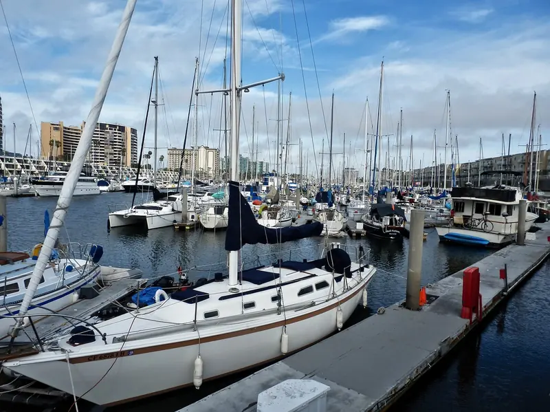 A sailboat at dock, with the harbour's waterfront apartment towers behind.