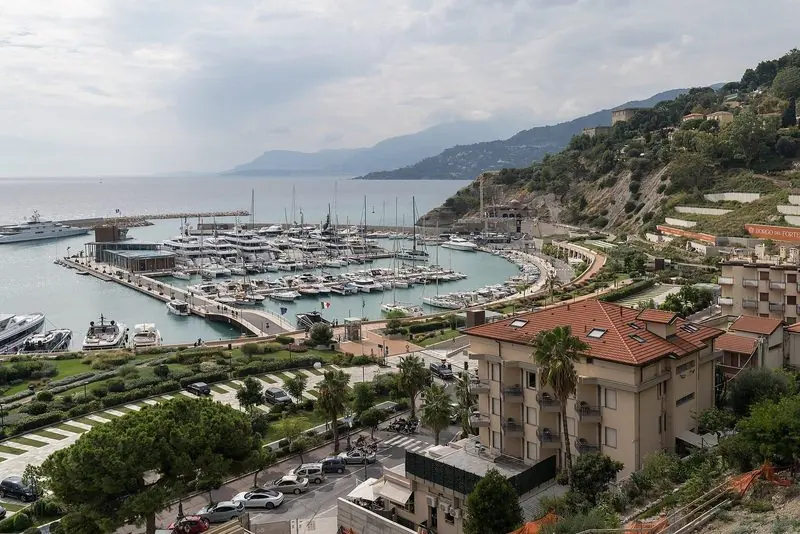 From the hillside the marina sits below the town with its breakwater arm curving round and the coast running west toward the French border.