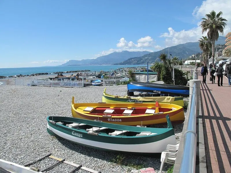 Wooden boats rest on the shingle along the town beach, with the promenade behind and the shore running east.