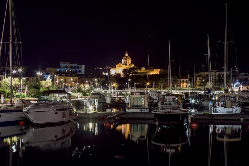 Marina di Loano by night, the hillside sanctuary of Monte Carmelo lit above the masts.