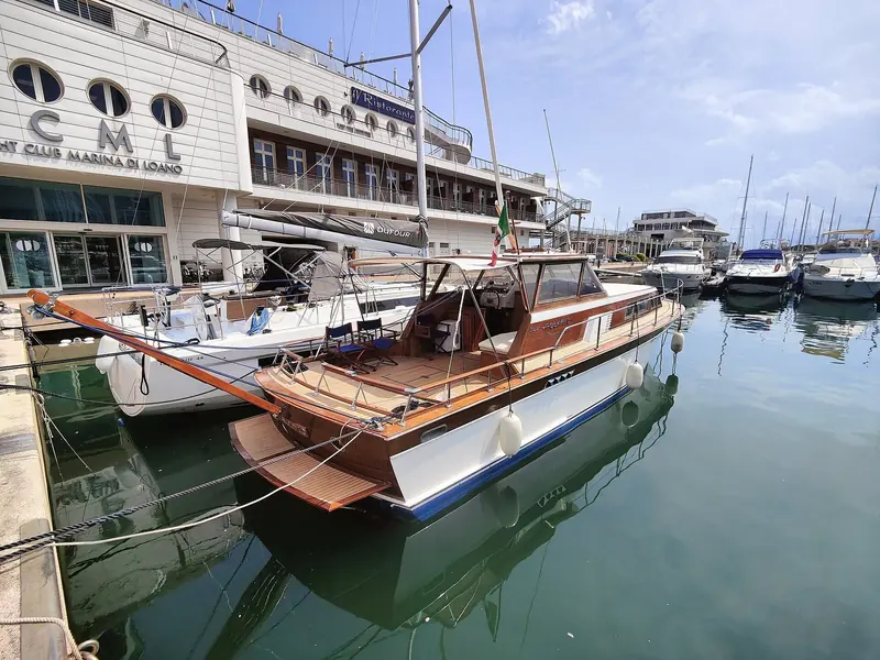 A classic wooden motor yacht moored on the quay outside the Circolo Motonautico Loanese clubhouse.
