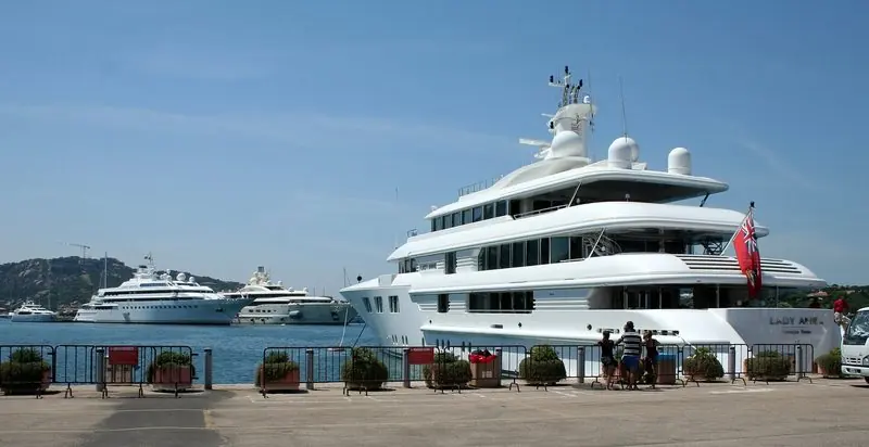 A large motor yacht sits on the superyacht quay with two more of her size lying off, the dock itself kept behind barriers.