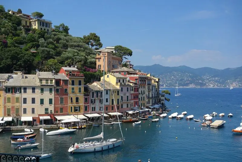 Portofino's bay opens north to the Gulf of Tigullio, with tenders and small craft on moorings in the middle and a sailing yacht lying off the painted waterfront.