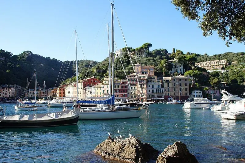 Sailing yachts lie to moorings across the width of the bay, the village and its wooded hillside standing directly behind the quay.
