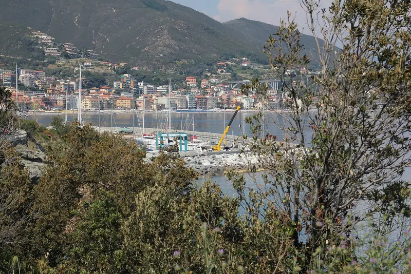 A working crane on the breakwater, with Varazze's town beach and seafront visible across the water.