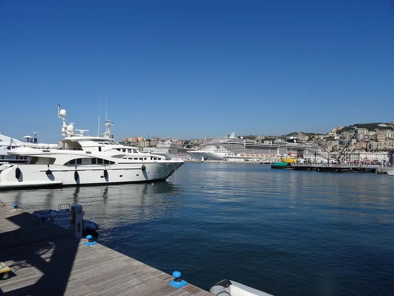 A motor yacht on the Porto Antico pontoons with the city rising behind the quay.