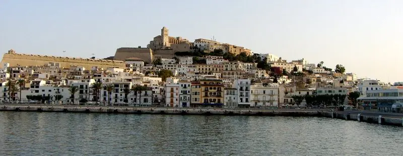 Seen from the water, the cathedral and its bell tower stand above the stacked white houses of Ibiza town and the palm-lined quay.