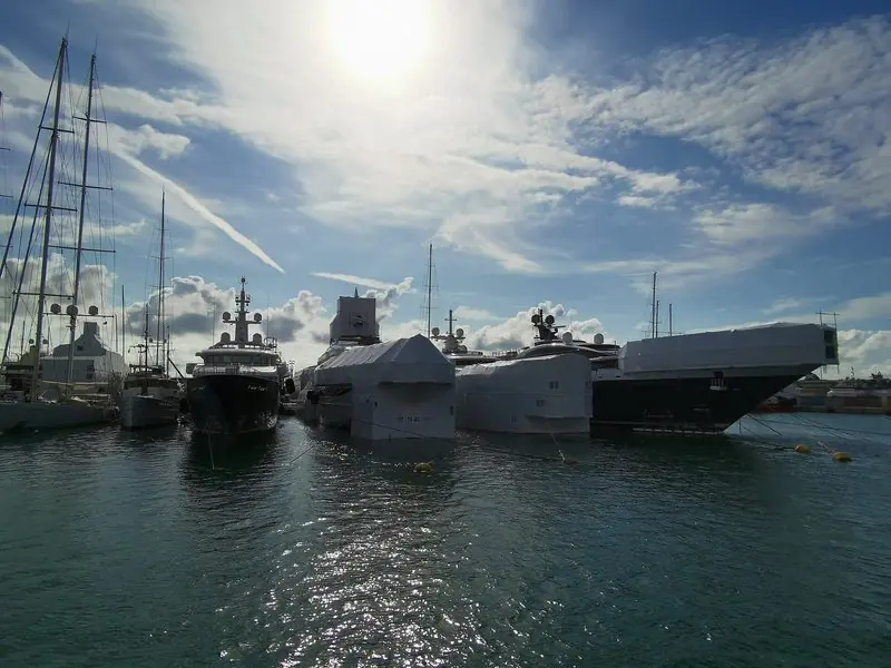 Winter refit season fills the inner quay, where a line of motor yachts sits shrink wrapped alongside a dark hulled expedition boat and a big rigged sailing yacht.
