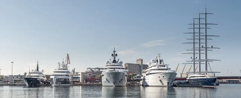 Five yachts lie across the basin, among them a three masted sailing yacht, with the grain silos and cranes of the commercial port behind.