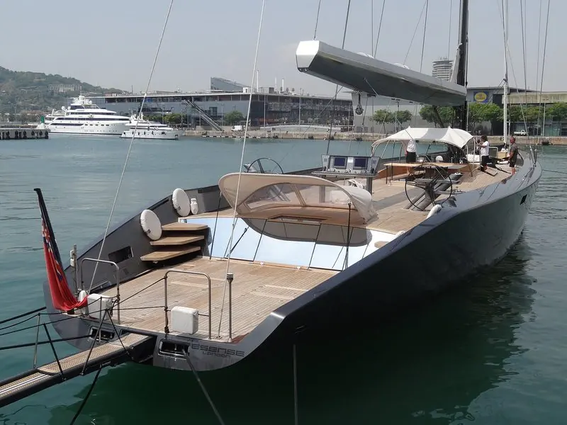 Flat water inside the breakwater lets a sailing superyacht lie stern-to off the port buildings, with Montjuic rising beyond.