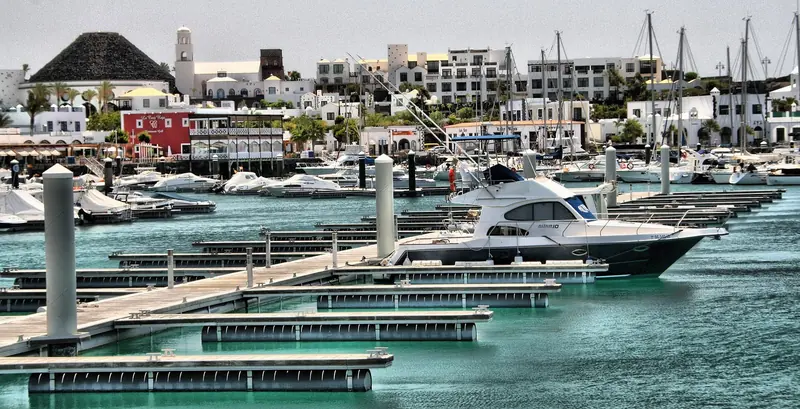 Marina Rubicon's berths and its own volcanic cone backdrop, with the Canarian-village retail centre climbing the hill behind.