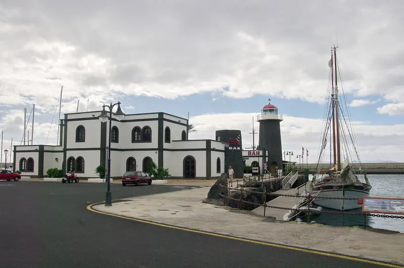 The marina's black-and-white capitania building beside its own black lighthouse and a tall ship alongside.