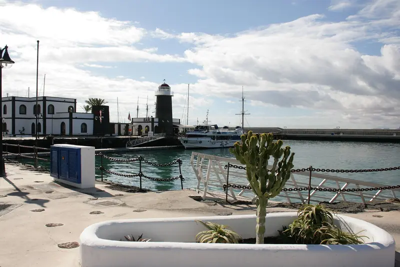 The lighthouse and a tour boat at the marina entrance, with a cactus planter typical of the village's landscaping.