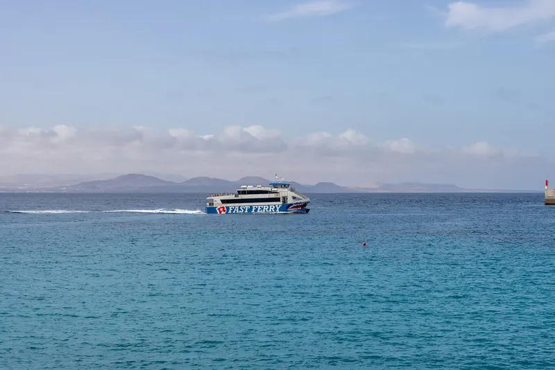 A fast ferry passes offshore, the kind of link that connects Playa Blanca to Corralejo on Fuerteventura.