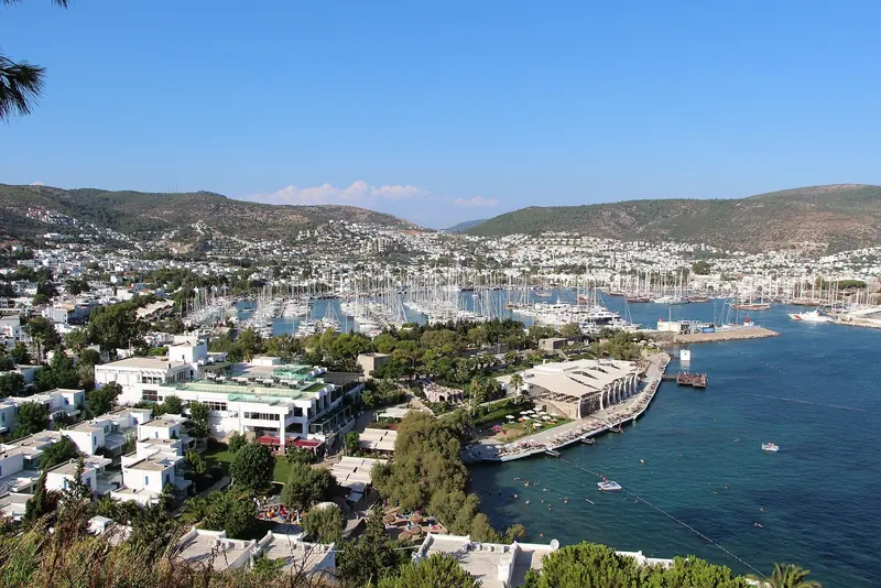 Bodrum from the hill above the town, the marina filling the western bay with the white town wrapped around it. The berths are in the middle of everything, which is the whole proposition.