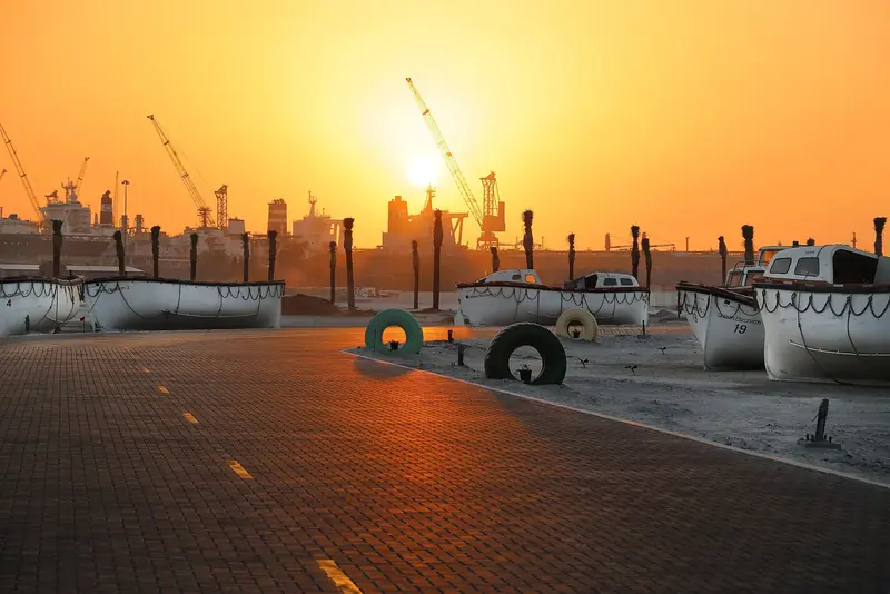 QE2's original lifeboats, preserved on the dockside near her berth at Mina Rashid, at sunset with the port's cargo cranes behind.