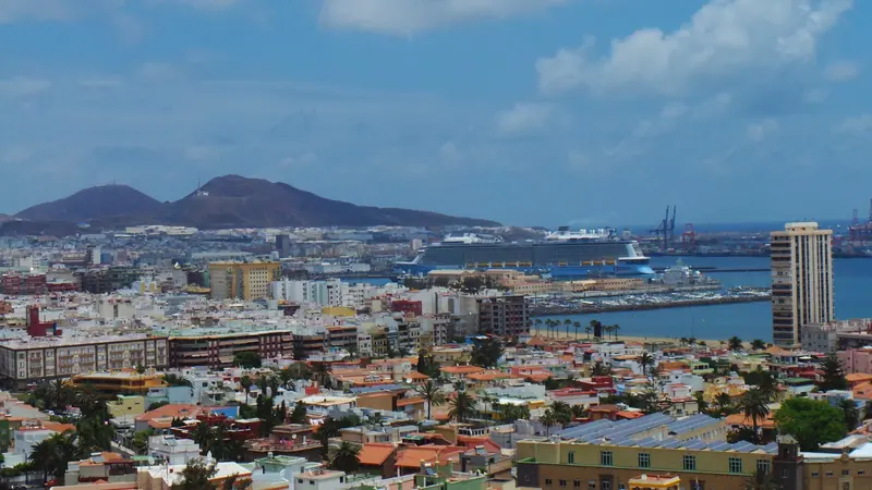 Las Palmas de Gran Canaria from above, the Muelle de Santa Catalina marina and cruise terminal on the near shore below the Isletas hills, a Royal Caribbean ship alongside.