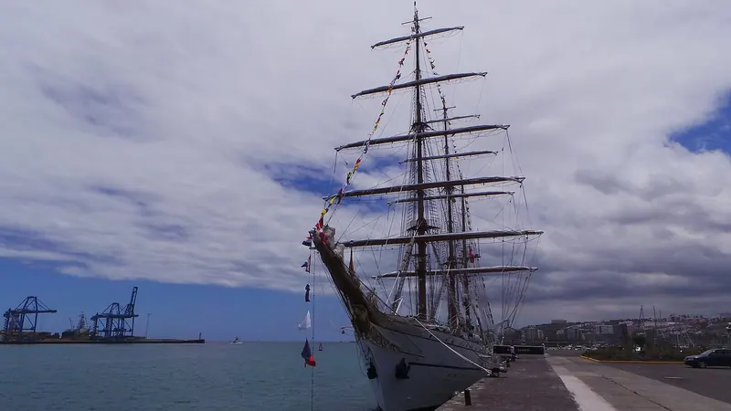 The Portuguese Navy tall ship Sagres dressed with signal flags at Puerto de la Luz, the container terminal's gantry cranes across the water.