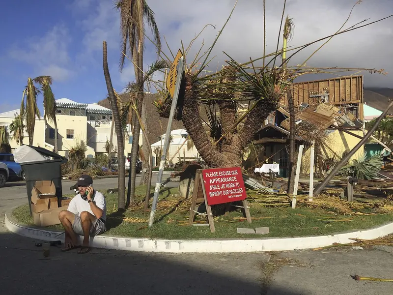 A man sits beside a Nanny Cay marina sign amid storm wreckage after Hurricane Irma crossed Tortola on 6 September 2017.