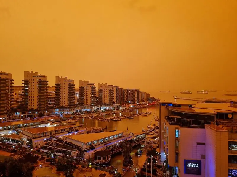 Evening light under Saharan dust turns the basin orange, the boardwalk bars and restaurants lit up along the waterfront directly beside the pontoons.