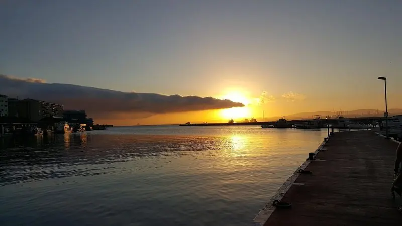 Looking west from the quay the sun drops behind the far shore of the bay, tankers lying on the anchorage and the marina's outer pontoon in the foreground.