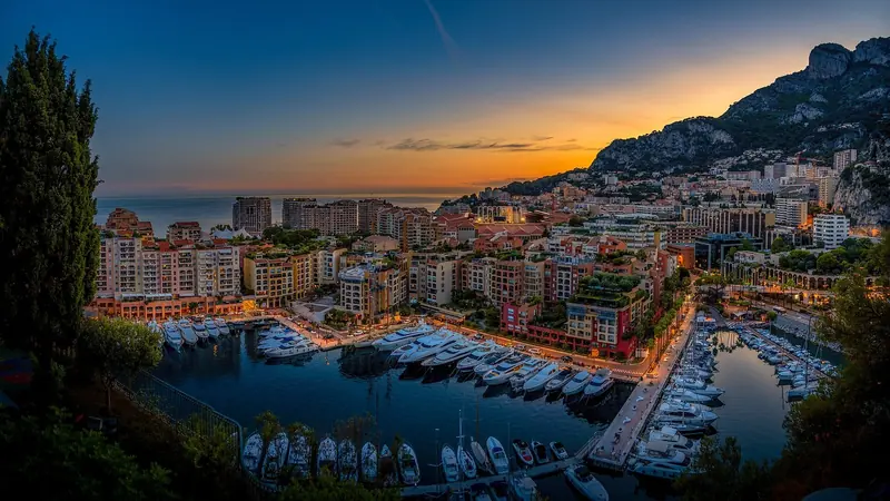 Fontvieille at dusk, the marina lit up against the dark hillside. The district was built on land reclaimed from the sea rather than carved from an existing bay.