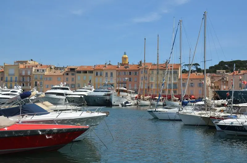 Motor yachts and sailing boats lie bows-to along both sides of the Vieux Port, the pastel quay houses and the bell tower standing directly behind them.