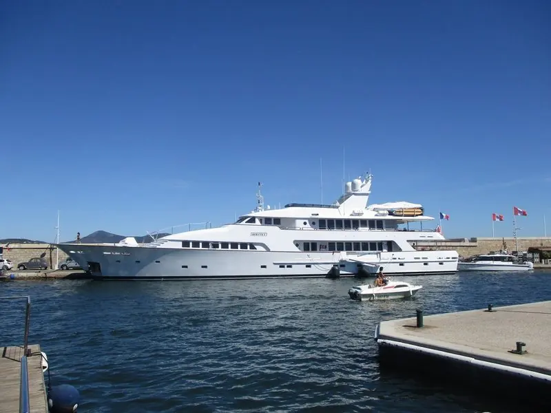 A white motor yacht takes the deep-water berth on the outer mole, clear of the crowd and open to the gulf beyond.