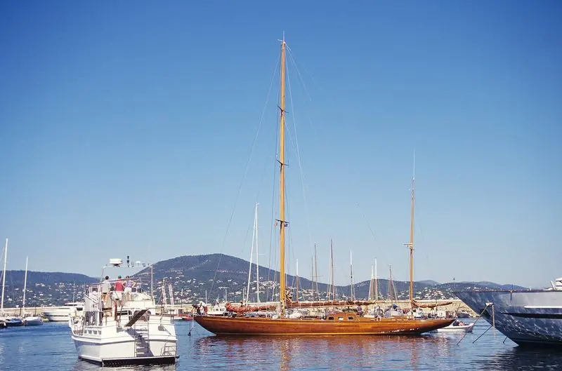 Under power a varnished wooden yawl works her way in past the moles, the hills of the Maures closing the far side of the gulf.