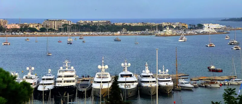 Motor yachts lie stern-to along the Cannes quay, with the bay and the Esterel hills behind. This is the view the address is bought for.