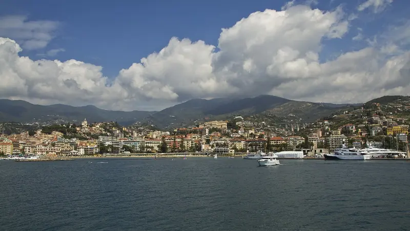 Sanremo's bay from the water, with Portosole's masts and a shrouded refit under way at the shipyard on the right, the old town and the hills behind.