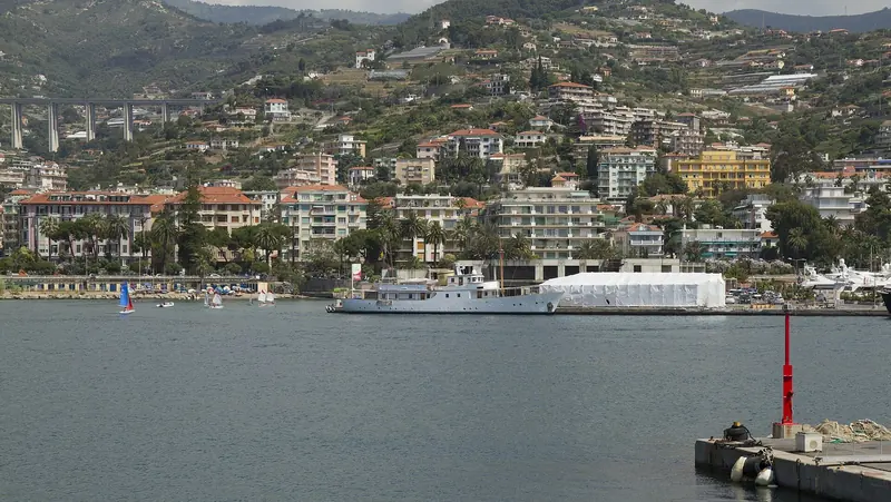 A yacht shrouded for refit work at the Portosole shipyard, dinghies sailing off the adjoining beach and the coastal viaduct behind.
