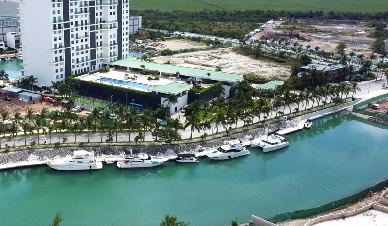 The canal-front berths beside the clubhouse and pool deck, with the next residential phase still under construction on the far bank.