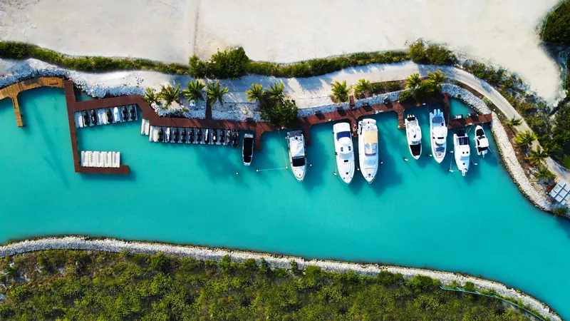 The Clubhouse Dock, a short curved pontoon between a sandy beach and the mangrove-lined bank, with a handful of smaller boats moored stern-to.