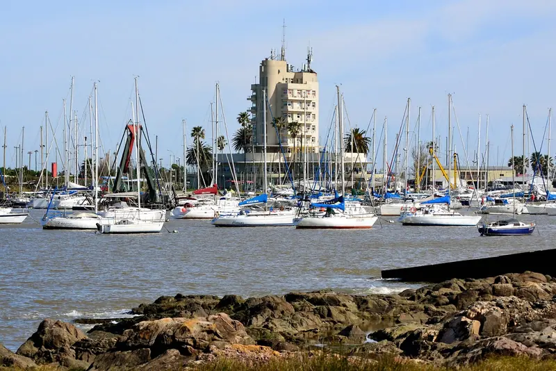 Yachts moored close to shore beneath the club's landmark tower, cranes and workshops visible along the quay.