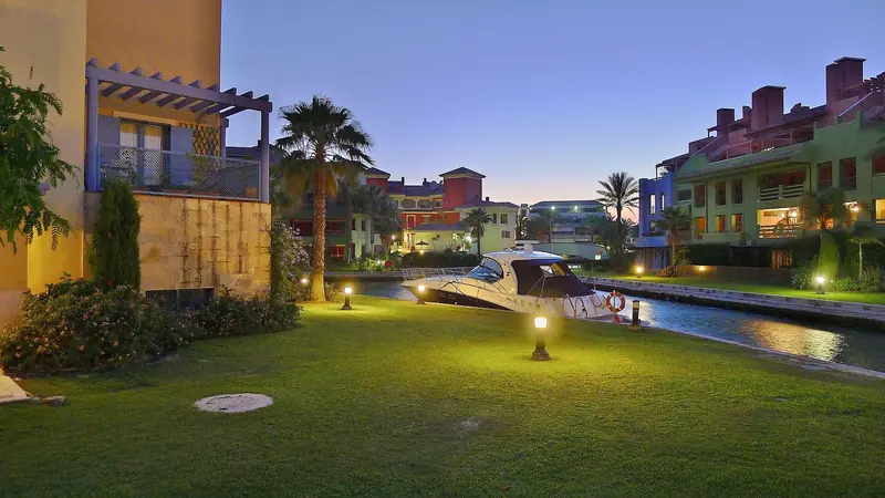 A sportfisher tied up on the grass-fronted canal behind a private villa at dusk, one of the residential berths that put a boat closer to the owner's own lawn than to any communal pontoon