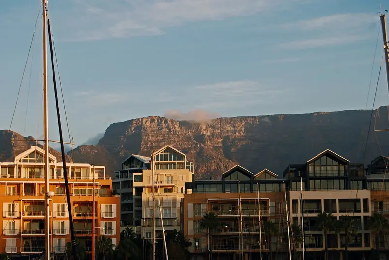 Yacht masts rise past the Waterfront's harbourside apartments at sunset, evening light catching Table Mountain's cliff face behind them.