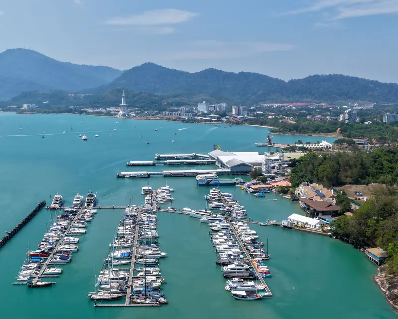 Royal Langkawi Yacht Club's marina basin from the air, its finger pontoons packed with sailboats and motoryachts, Kuah town and the Eagle Square monument behind.