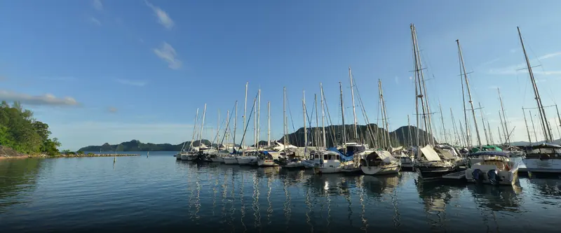 Cruising sailboats moored bow-to at first light on a quiet pontoon, the outer islands visible across calm water.