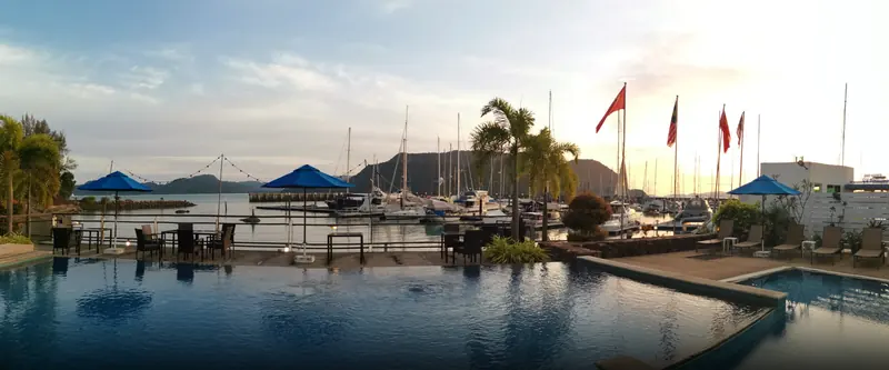 The clubhouse infinity pool at sunset, national and club flags flying over the pontoons and moored yachts beyond.