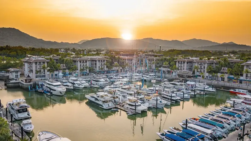 Royal Phuket Marina's basin at sunset during a yacht show, the marina's own Sino-Thai waterfront apartment blocks lining both sides of the canal-like berthing basin.