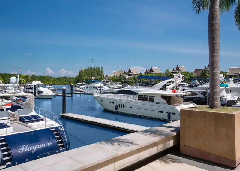 A motor yacht on a finger berth at the marina's wet-berth pontoons, Royal Villa rooftops visible across the water.