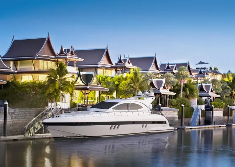 A yacht alongside a Royal Villa's private dock at dusk, the pavilion-roofed waterfront villas that give this marina its residential character.
