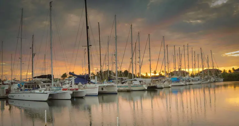 Sunset over the basin, masts of yachts staged for a canal transit reflected in still water.